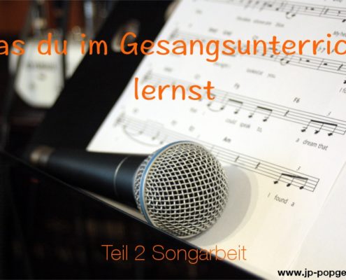 Songarbeit lernst du im Gesangsunterricht. Als Beispiel dafür zeigt das Bild ein Mikrofon und Noten, die auf einem Notenständer liegen.