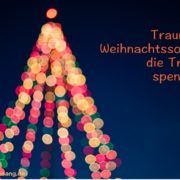 traurige Weihnachts Songs Das Bild zeigt verschwommen die Lichter an einem Weihnachtsbaum vor dunklem Himmel.