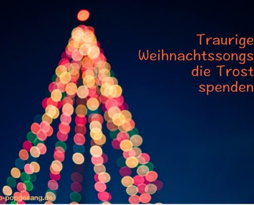traurige Weihnachts Songs Das Bild zeigt verschwommen die Lichter an einem Weihnachtsbaum vor dunklem Himmel.