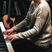 Die Stimme verbessern geht übers Tun, wie diese Frau im grauen Pulli, die am Klavier sitzt und spielt