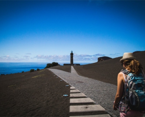 Eine Frau mit Rucksack an einer Kreuzung. Die Ziele sind ein Leuchtturm und das Meer.