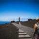 Eine Frau mit Rucksack an einer Kreuzung. Die Ziele sind ein Leuchtturm und das Meer.