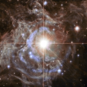 Ein leuchtend weißer Stern, im Hintergrund eine grau-blauen Gaswolke und schwarzes Universum mit weiteren Sternen.