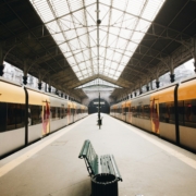 2 gelb-graue Züge stehen in einer Bahnhofshalle, der Bahnsteig ist leer.